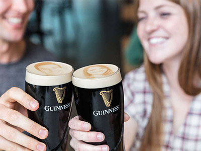 Two people clinking their personalised pints of Guinness with their selfie on at the Guinness Factory Tour with STOUTie in Dublin