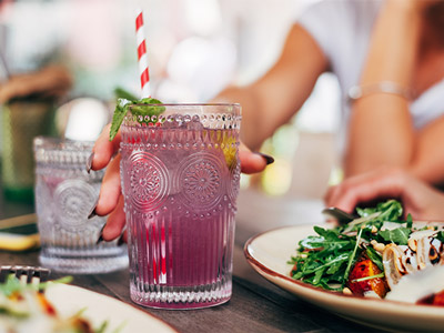 A pink cocktail with a mint leaf next to plates of food at Oasis Brunch in Benidorm