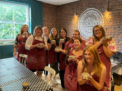 A group of women holding pottery up at a Cheeky Pottery Class in Brighton
