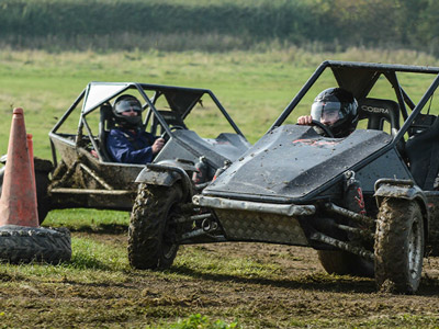 Two people in separate off road buggies driving round cones in a field