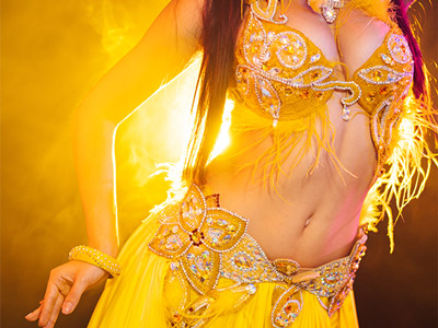 A close up of a woman belly dancing with a yellow outfit on and yellow lighting behind her