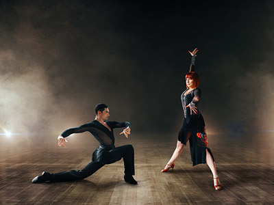 Two people salsa dancing with a dramatic dark background