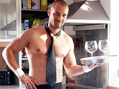 A topless man wearing nothing but a tie and apron with two drinks on a tray