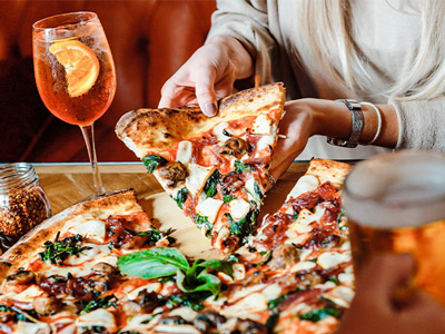 Someone pulling away a large slice of pizza with drinks on the table at Box