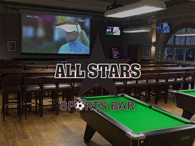 A pool table in front of a screen with sports on at the All Stars Sports Bar
