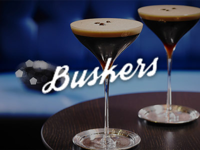 Two espresso martinis on a wooden table with the Buskers on the Ball logo overlayed 
