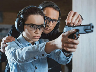 A woman aiming a gun with help from someone at Poznan shooting