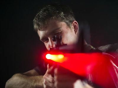 A man shooting a red laser towards the camera from a laser quest gun 