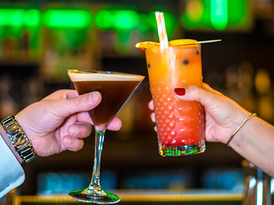 Two cocktails clinking with green lights in the background