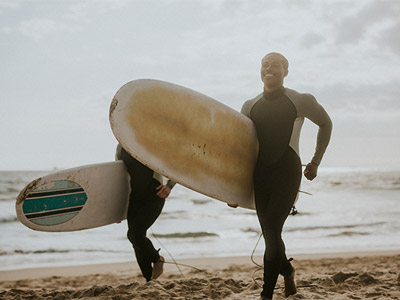 Two people wearing wetsuits carrying surfboards 