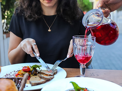 A glass of sangria being poured while a woman enjoys her meal