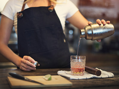 Someone making a cocktail and pouring it into a glass