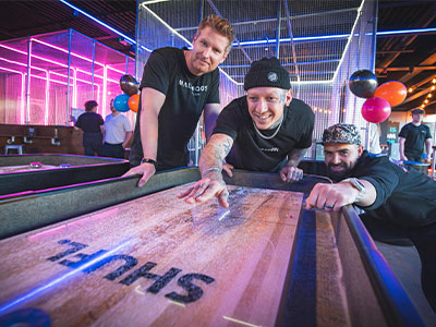 Three men playing shuffleboard at Boom Battle Bar 