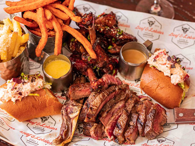 A platter of food including sliced beef, chips, a lobster sandwich and a couple of different sauces 