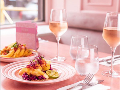 Two pink plates with brunch dishes on them next to two glasses of alcohol 