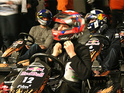 A man driving a go kart in helmet and overalls, on an indoor track