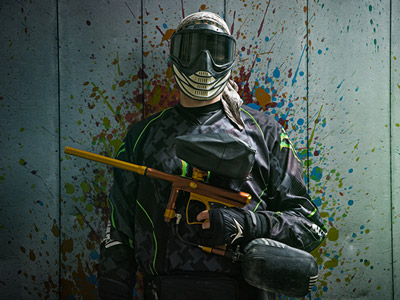 A man in a paintball mask and camouflage gear, aiming with a paintball gun