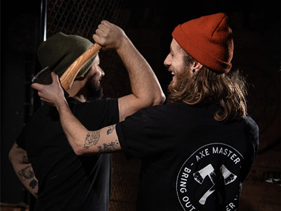An axe throwing instructor showing a man how to throw his axe over his shoulder 