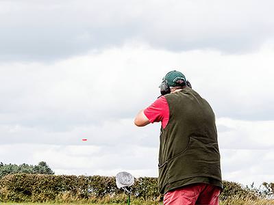 A man aiming a shotgun into the sky, with an orange clay visible