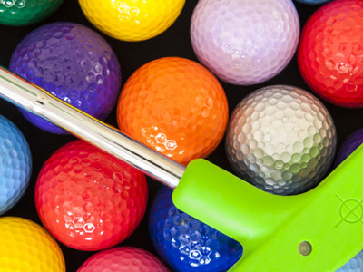 Loads of golf balls that are different colours with a golf putter laying on top 