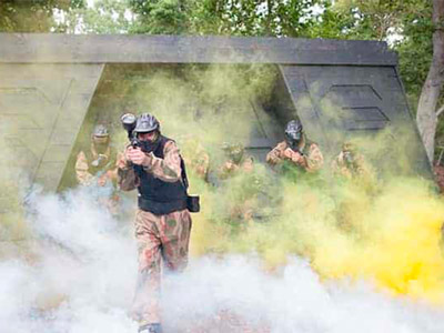 A man appearing out of some smoke with a paintball gun in hand