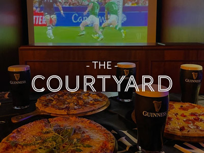 A table of pizzas and Guinness facing towards a screen showing live sport with the words The Courtyard layered over it 