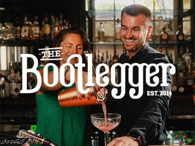 A bartender teaching a woman on a hen do how to make a cocktail with the Bootlegger logo layered over it 
