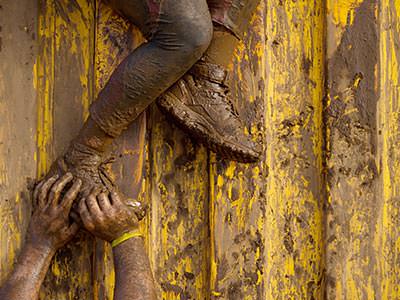 A person's muddy hands pushing another person's muddy legs over a wall