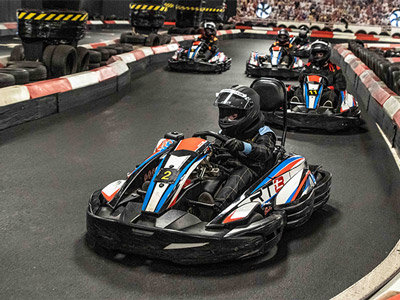 A group of people racing in go karts in an indoor venue 
