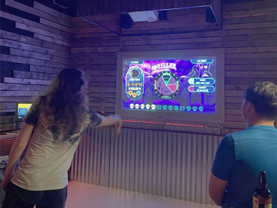 Someone with long hair throwing a dart at a darts board where the game is called Killer 