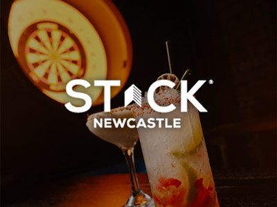 A darts board with some drinks in the foreground that has the STACK logo layered over it 
