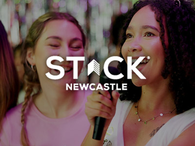 Two women singing into a microphone with the STACK logo layered over it 