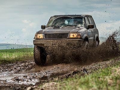 A 4x4 vehicle driving down a dirt track with a person standing nearby