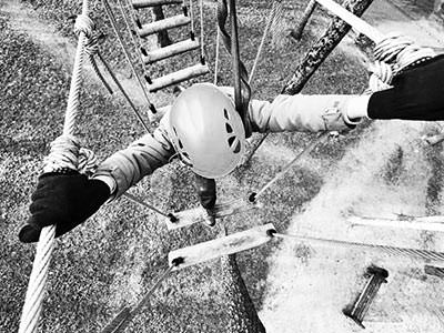 Black and white image of a woman walking along a rope bridge above the ground