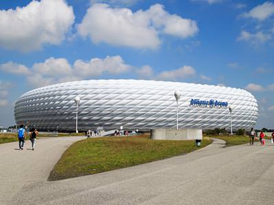 White exterior of the Allianz Arena, with grounds and people in foreground