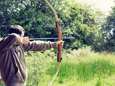 A close up of a man firing a bow and arrow in a field