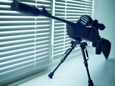 A close up of an air rifle on a stand in front of a window with the blinds shut