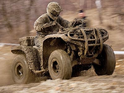 A man covered in mud, driving a quad bike