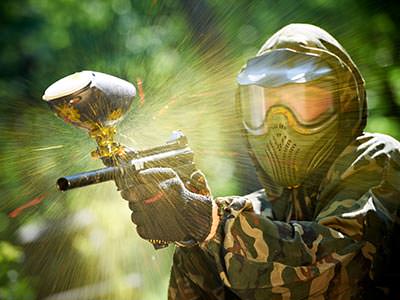 Close up of a man firing a paintball gun whilst wearing a mask and camouflage gear