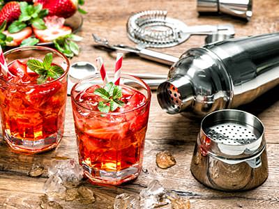 Two cocktails, freshly made, with cocktail making ingredients lying out on a wooden table 