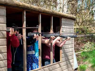 Four people aiming rifles at can targets outside at Rifle Shooting