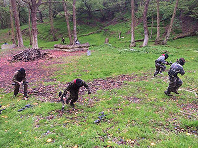 Four people running in a wooded area with paintball guns in their hands
