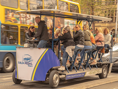 A pedal-powered bus on a road with passengers