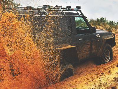 A 4x4 vehicle with its rear wheels bogged down, spraying orange muddy water out behind it