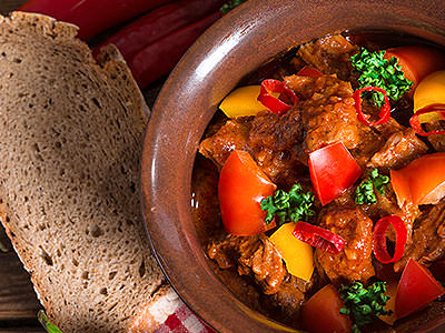 Some traditional food in a brown bowl, with some bread lying next to it 