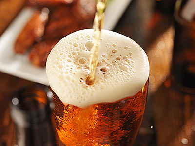 A pint of beer being poured, with a very frothy head