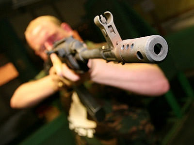 A man wearing camouflage and aiming his gun just beyond the camera
