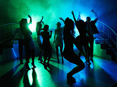 Silhouettes of people dancing in a club, under green and blue disco lighting 
