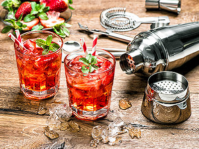 Two cocktails, freshly made, with cocktail making ingredients lying out on a wooden table 