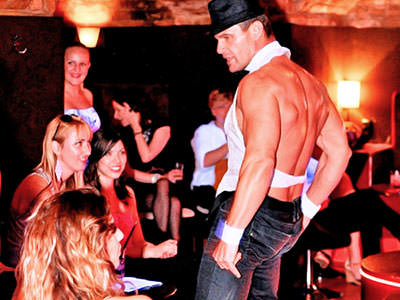 Close up of a male stripper in jeans, standing in front of a group of women sat down